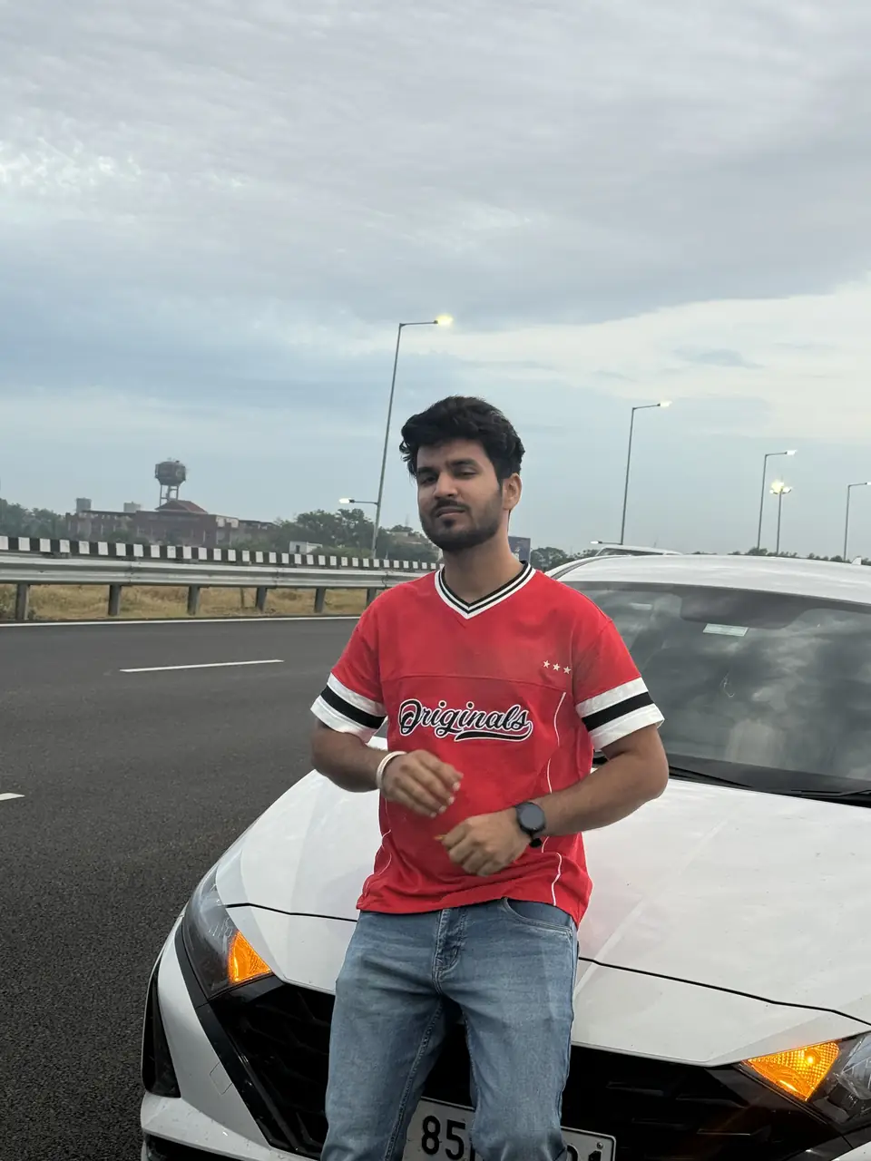 Pritish Bhatti in a red t-shirt sitting on the hood of a car
