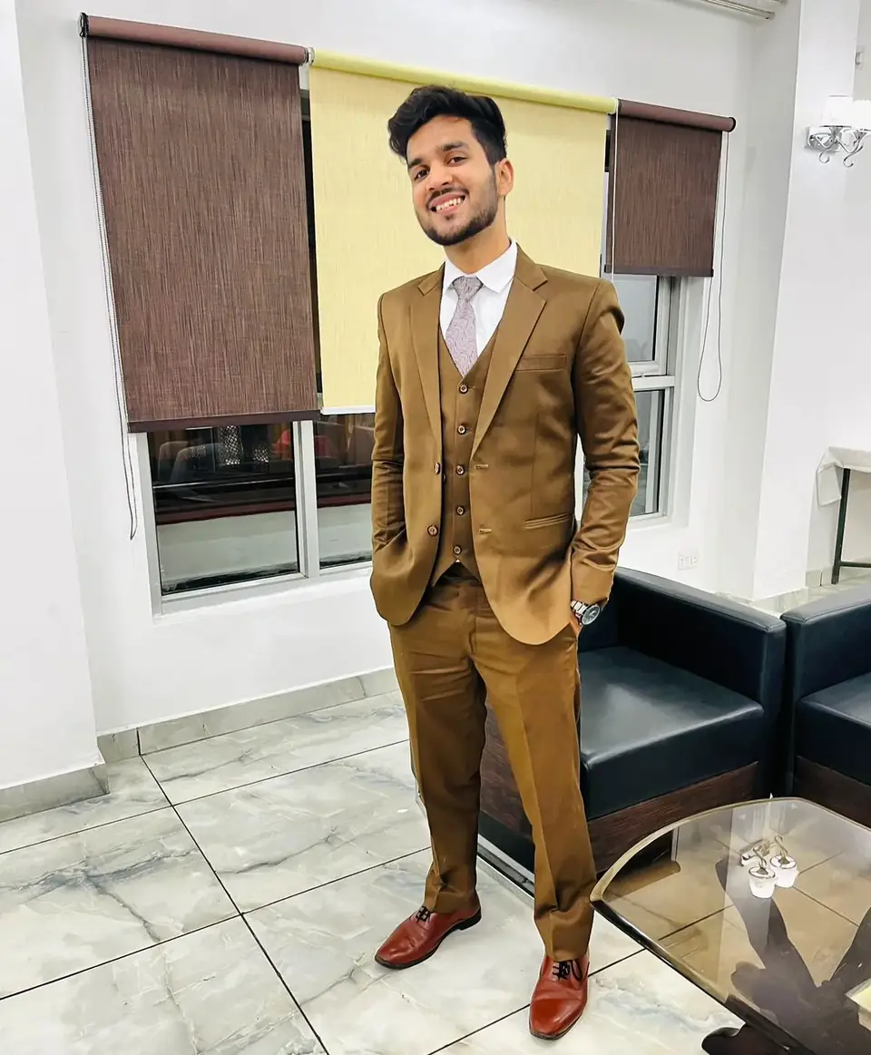 Pritish Bhatti in a brown three-piece suit standing in warm interior light